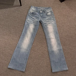 Lågmidjade bootcut  - Ljusblå lågmidjade bootcut med vita detaljer. Midjemåttet är 32,5cm och innerbenslängen är 79cm. Hör av dig vid frågor💗
