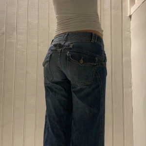 Lågmidjade jeans  - Lågmidjade vida jeans med en liten vit målarfläck på ena bakfickan. Knappen sitter också lite löst men kan sys fast.