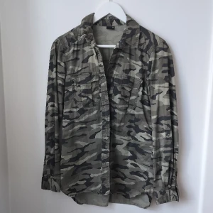 Militärgrön kamouflage-skjorta strl 34 - Mycket mer militärgrön irl (tyckte bilderna blev aningen gråa). Supersnygg till skjorts på våren/sommaren. Storlek 34 men aningen oversized.