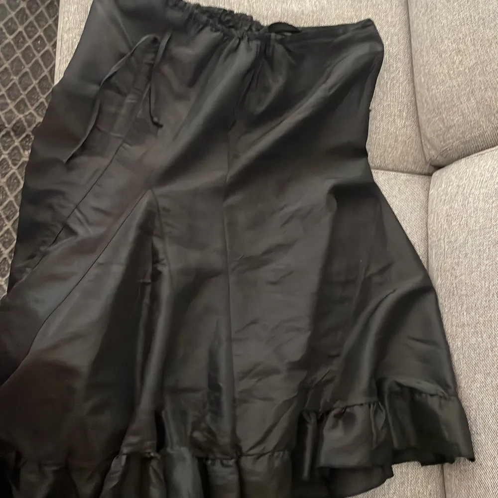 En lång svart kjol med luftigt skönt material och en dragkedja på sidan. Passformen och längden är reglerbar med ett snöre på sidan. Den är köpt second hand för några år sedan men aldrig använd för den är för liten. Skulle  säga att den passar M - L.. Kjolar.