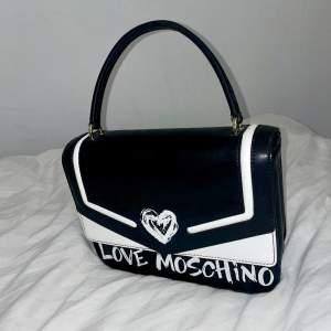 Säljer nu en helt oanvänd designer väska ifrån Love Moschino, köpt på Zalando för ett år sedan men aldrig använd. Längre band följer också med. Svart/vit väska med röd lyxig insida.  Kan skickas.  