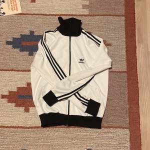 Vit adidas kofta  - Vit adidas kofta. Säljs på grund av att den är lite för liten för mig på 178. Koftan har några små fläckar som knappt syns när väl tröjan är på (skicka för bilder)