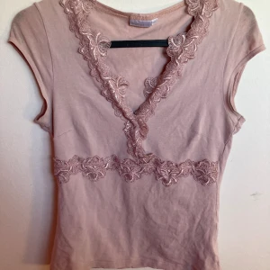 Blommig topp - Urringad med spetsblommor, figursydd i superskönt material. Skulle säga att den är mer rosa i verkligheten. 