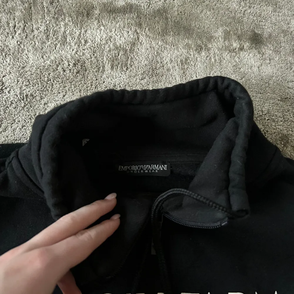 En svart polo hoddie utan luva med ull på insidan från Emporio Armani. Text (märket) på framsidan av tröjan. . Hoodies.