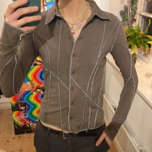 Skjorta - Grön/brun/grå tajt skjortaktig topp från Weekday med synliga sömmar i grå/blå färg. Endast använd en gång och väldigt stretchigt material. Storlek S.