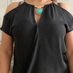 Svart blus. - Blus i viskos tyg, storlek M. Med detaljer i blåa och guldfärgad  Bra skick.