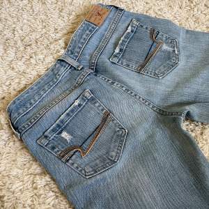 American Eagle jeans i lågmidjad och bootcut modell med snygga detaljer och slitningar. ❤️ Innerben: 73cm, midja rakt över: 36,5cm. Jag är 167. Meddela vid önskan om fler mått! 🫶 Perfekt skick förutom att de är uppsydda. 🥰 Säljer fler vintage jeans! ❤️