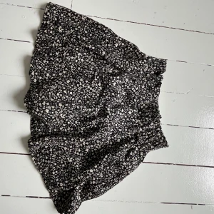 Blommig kjol från Zara  - Jättesöt kort kjol. Svart kjol med vita blommor, ”innershorts”. Storlek 140/ 10-11 år