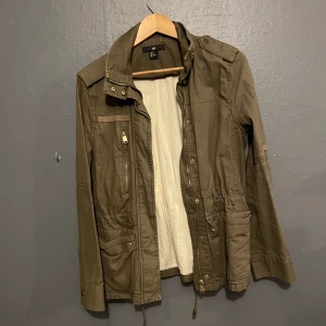 Vårjacka  - Militärgrön vårjacka, figursydd med snöre i midjan. Jätte skön och super snygg på, säljer pga har alldeles för mycket jackor. Storlek 36 från H&m