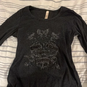 Långärmad tajt tröja  - En långärmad mörkgrå tröja, med tryck och paljetter på framsidan. Märket heter ” Ouí Moments ”. Det står ingen storlek men är ungefär en S. 