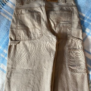 Baggy jeans  - Cargopants I storlek 30 köpta på beyondretro. På bilderna ser de randiga ut men det är bara kameran, de är som på bild två. Aldrig använt de då de var lite stora i midjan. Midja: 79cm, innerbenslängd: 80cm. Skriv för fler bilder eller mått. Nypris 500kr