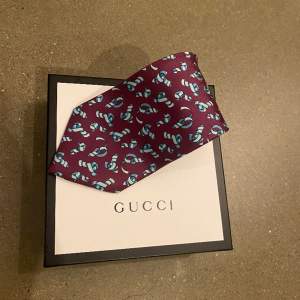 En stilren Gucci slips i en snygg vin röd färg med turkosa mönster. Bra skick. Självklart Äkta. Slipsen är 140 cm lång. (Box ingår ej men kan köpas till)  Hör av er vid frågor eller funderingar! 👔