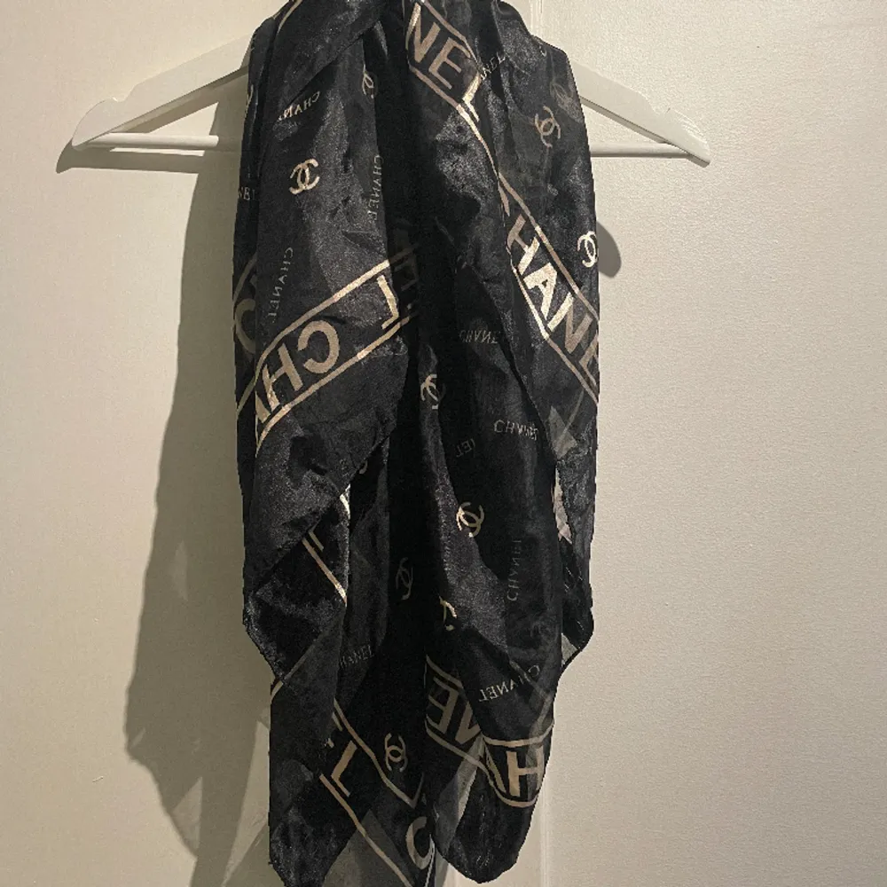 Second hand scarf med Chanel tryck i svart och guld. Finns slitningar se sista bilden. Använt som scarf/topp/utsmyckad på väska etc. . Accessoarer.