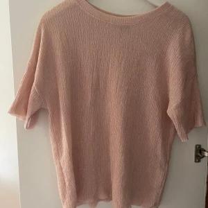 Ljusrosa tröja  - En ljusrosa tröja med korta ärmar och en rund halsringning. Tröjan har en lös passform och är tillverkad i ett texturerat material. 🌸💗✨