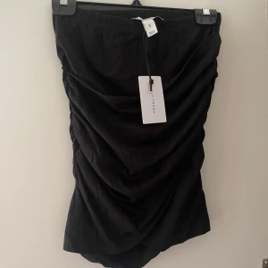 Svart kjol - Säljer denna eleganta svarta kjolen från Nelly med draperade detaljer. Kjolen är kort och har en tight passform, vilket gör den perfekt för festliga tillfällen. Aldrig använd✨🖤🤍
