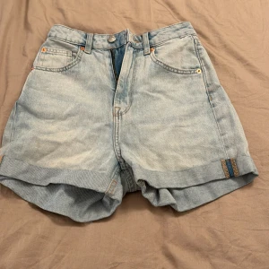 Ljusblå jeansshorts - Ett par ljusblå jeansshorts med uppvikta ben och klassisk femficksdesign. Shortsen har en knapp och dragkedja framtill samt bälteshällor.