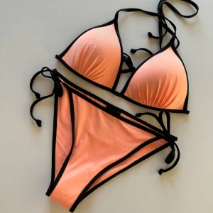 Korall orange bikini 👙  - Superfin oanvänd bikini med svarta snören, till sommaren! Överdelen är i storlek 38 och underdelen alltså trosorna är i storlek 34, man kan justera hur man vill den ska sitta genom att knyta snörena
