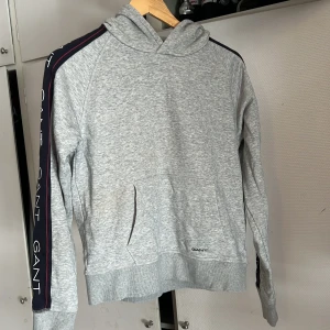 Grå gant hoodie - En grå gant hoodie me gant text på armarna, storlek 16years men den är som s