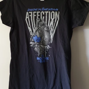 Svart T-shirt, backstage club, EMP - T-shirt  Storlek: uppskattas som en S eller liten M. (Står L på lappen, men väldigt liten I storlek).  Skick: max använda en gång  Färg: svart med lila detaljer Märke: EMP Backstage club  Längd: ca 67cm, axelbredd: ca 35cm 