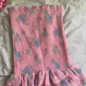 Säljer en superfin rosa kjol från Bikbok med blommigt mönster i lila och grönt. Den har en volangdetalj längst ner.. Den är i nyskick och väldigt bekväm att ha på sig. Passar perfekt för dig som vill ha en söt och somrig look! Den är stretchig så den formas utifrån er kropp