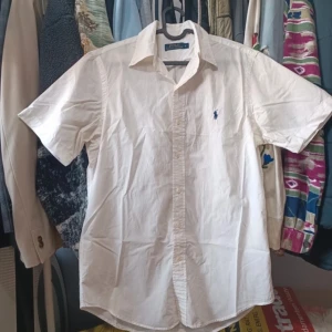 Vit kortärmad skjorta från Polo Ralph Lauren - Säljer en snygg vit kortärmad skjorta från Polo Ralph Lauren. Skjortan är i bomull och har en klassisk krage med knappar. Den har en broderad blå logga på bröstet som ger en stilren touch. Perfekt för sommarens alla tillfällen! Köp direkt eller ge prisförslag 💛