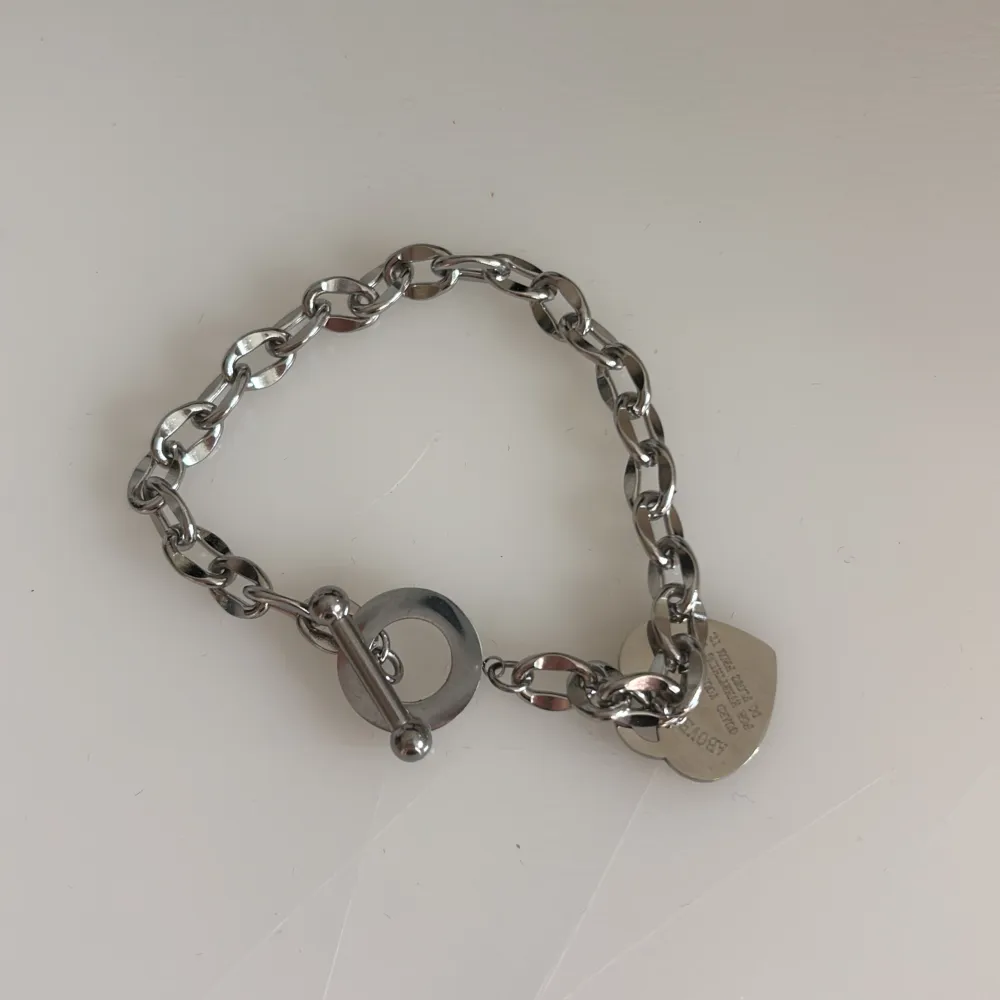 Säljer ett snyggt silverfärgat armband med ett hjärthänge. Armbandet har en robust kedja och ett hjärthänge med ingraverad text. Perfekt för att ge en elegant touch till din outfit. Köp direkt eller ge prisförslag 💛. Accessoarer.