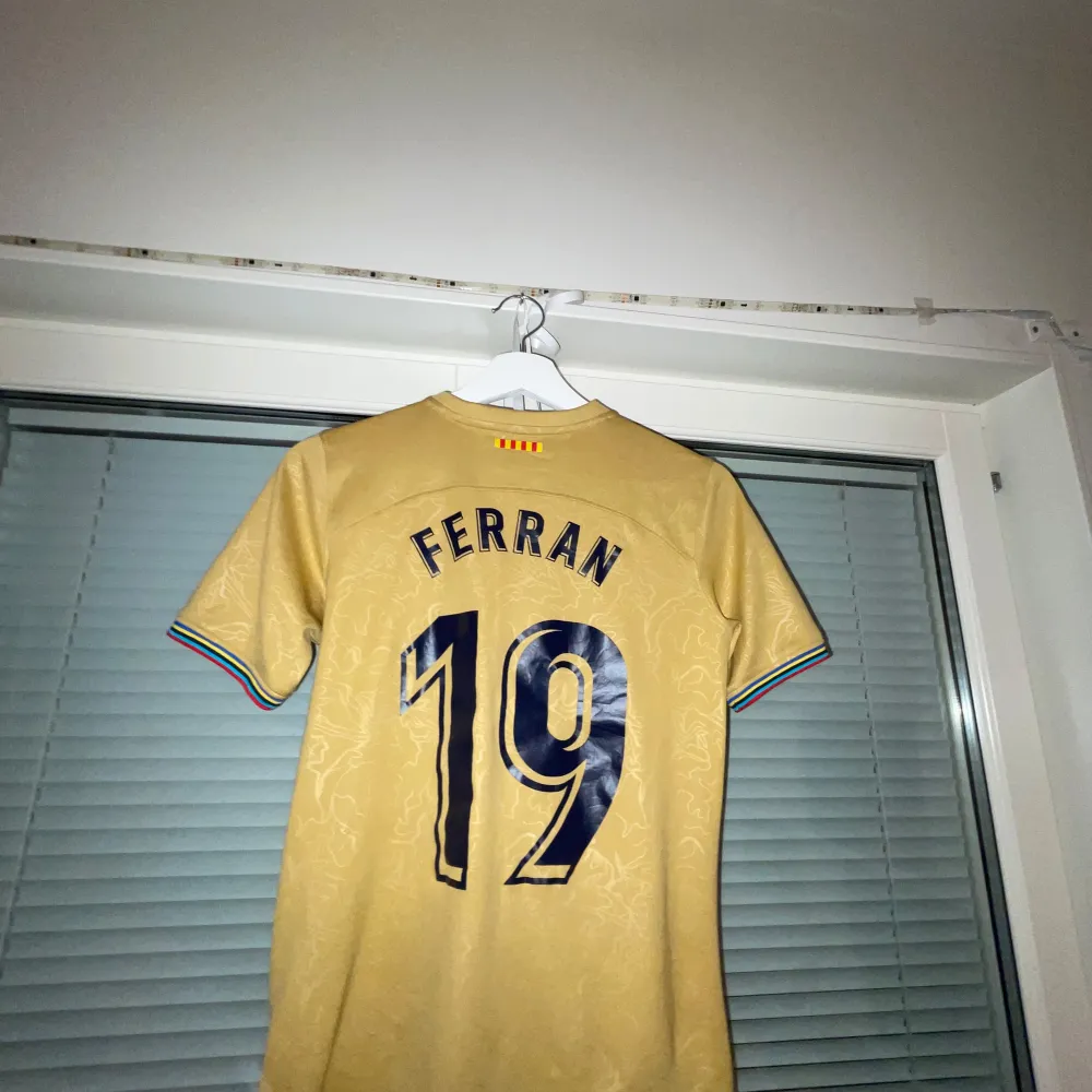 Säljer en guldig Barca. Tröjan har ett tryck med 'Spotify' på framsidan och 'Ferran 19' på baksidan. Den har också färgglada detaljer vid ärmsluten. Perfekt för Barca fans. T-shirts.