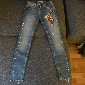 Zarajeans med nitar och blommor - Storlek 34, oanvänd, köpt i Spanien, 93 cm lång 