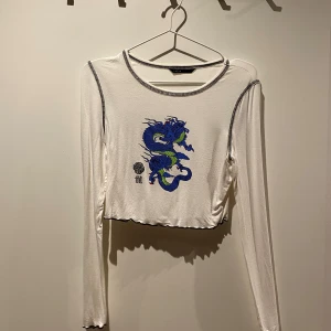 Kroppad top från Sheln - Kroppad top i vit med drak-print. Står storlek M/38 i tröjan men den är mer som s
