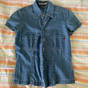 Jeansskjorta från Original by Carl Gry - En jeansskjorta med korta ärmar från Original by Carl Gry. Skjortan har två bröstfickor och knappar framtill. Den är tillverkad i jeansmaterial och har en klassisk krage.