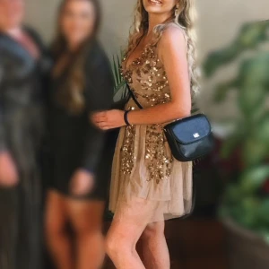 Glittrande festklänning - Säljer festklänning från Maya med paljetter och pärlor i guld, brons och brunt.  • Djup V-ringad urringning • Täckt rygg i meshtyg • Slutar ovanför knät på mig som är 169 cm lång • Använd 1 gång  • Originalpris: 1599kr 