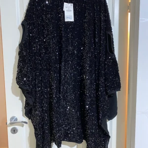 ZARA cape/poncho - En svart poncho i paljetter från Zara. Har ärmar. Är en stickad poncho med paljetter (se bild) så den är varm. Helt ny, prislapp kvar. Nypris 1000 kr.  Strl M. 