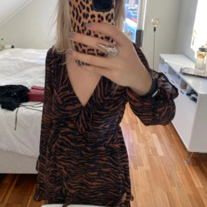 Klänning i djurmönster - Säljer denna snygga klänning i tigermönster. Volang. En knapp kan justera skärningen vid bröstet.