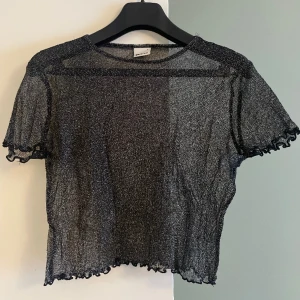 Meshtopp - Meshtopp i svart med glittriga inslag. Storlek S. Köpt på Gina Tricot. Kortärmad och kort midja. I gott skick. 