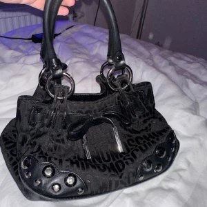 Moschino handväska  - Säljer min vintage moschino handväska som inte längre kommer till användning. Har inte använt den på ett tag och är i bra skick! Har dock ett litet hål i en av fickorna, men inget man tänker på eller som syns utåt 