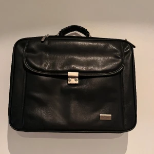 Svart Portfölj/dataväska  - En svart portfölj/dataväska där allt får plats med smidiga fack. Svart i läder, har även ett axelband