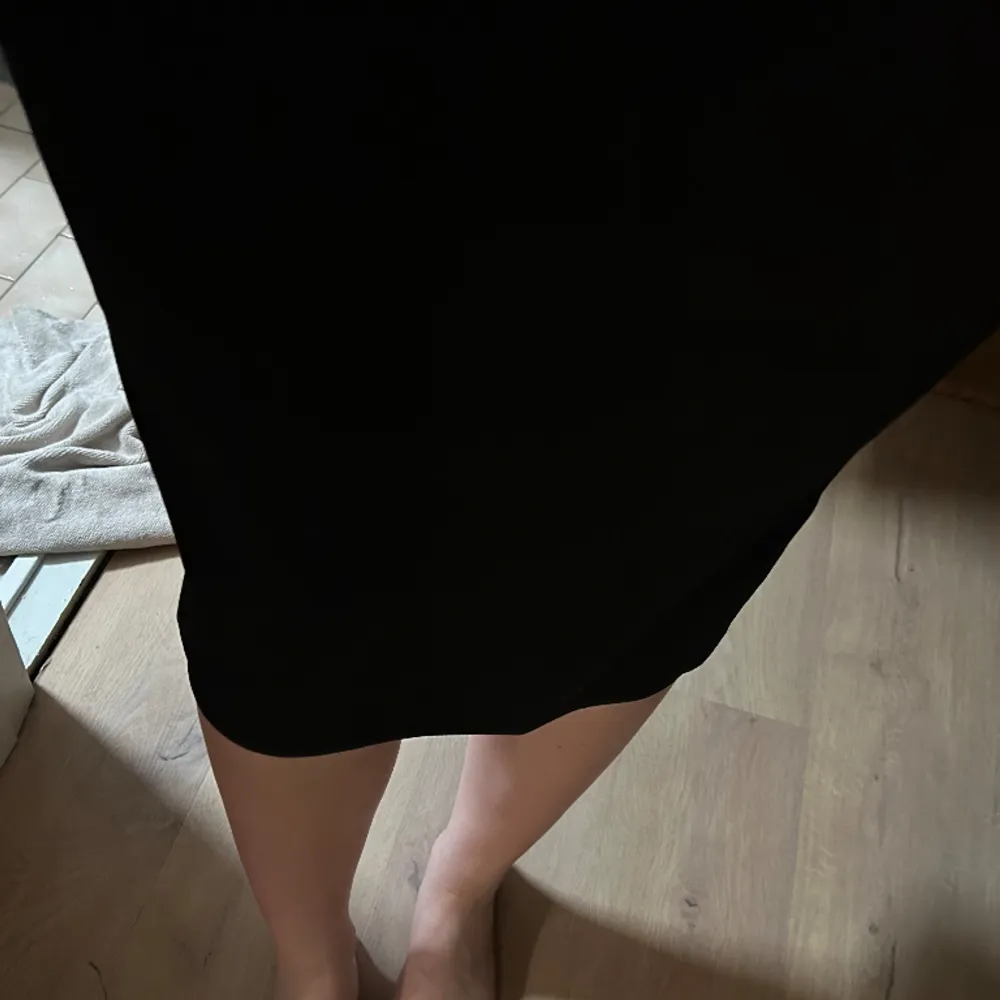 En svart klänning med detalj över bröstet.. Klänningar.