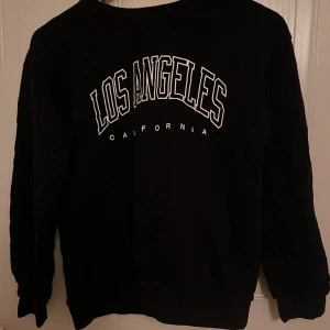 Svart sweatshirt  - En svart tröja med en vit text 