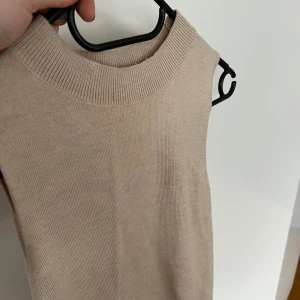 Stickad topp utan ärmar - Superfin beige stickad topp utan ärmar och med högre krage. Sitter väldigt fint på kroppen  Exklusive frakt
