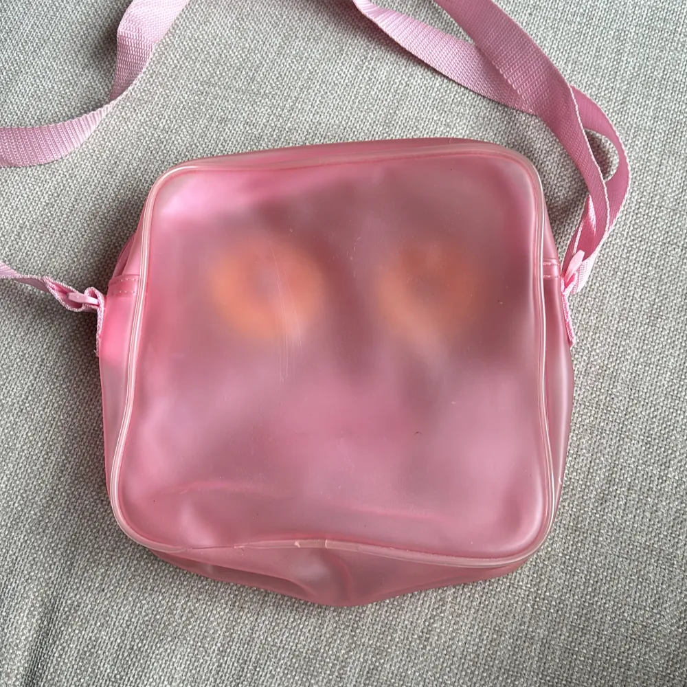 Söt väska i rosa genomskinligt plast-material. Genomskinligt fack med Hello Kitty på framsidan. Stort fack med dragkedja. Justerbar axelrem. Storlek ca 22x22 cm. Väskor.