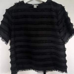 En svart blus / t-shirt med ”fransar”.  Rak passform.  Använd ett fåtal gånger, från H&M i stl 36. 