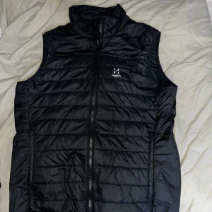 Haglöfs väst - Superbra skick, insidan är 90% dun och 10% fiädrar. Den är varm vadderad och regntålig. Det finns 2 handfickor på utsidan och även insidan. Elastiska ärmhål och nederfåll som ger bra värmeisolering och en bekväm passform.  