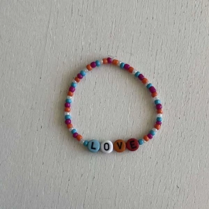 Egengjort pärlarmband  - Ett egengjort pärlarmband med färgerna blå, orange, magenta och vit. Armbandet har pärlor med bokstäver som avbildar ordet ”Love”. 