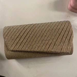 Väska - Guldig/champagne färgad väska som passar perfekt till bal. Går att ha både med och utan kedja. Köparen står för frakten.