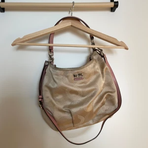 Coach Väska - Säljer nu min älskade Coach-väska då den förtjänar att bli använd! Inköpt på Tradera för ungefär ett år sedan. Säljaren sa att den var äkta och den har ett äkthetsmärke, men är inte 100% säker. Är beige/rosa/champagne i färgen. Fint skick