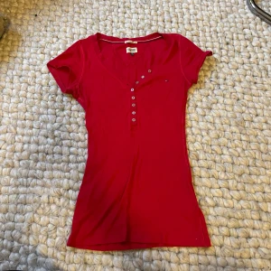 Hilfiger t-shirt  - Röd ribbad åtsittande t-shirt från Hilfiger. Strl xs-m då den är väldigt stretchig och mjuk. Två egna knapphål är gjorda men syns knappt.