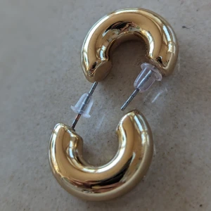 Guldfärgad örhängen i acrylic material  - Sparsamt använd  I mycket fint skick   Örhängen bredd ca 2 cm 