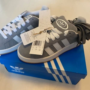 Nya Adidas Campus 00 storlek 37 1/3 - Adidas Originals Campus 00s j Storlek: 37 1/3 Färg: Grey Three / Cloud White / Cloud White ( gråa med vita ränder )  Ingår både gråa och vita skosnören.   Nya och oanvända. Ligger kvar i kartong. Köpta i Sverige och inte en massbeställning utomlands.