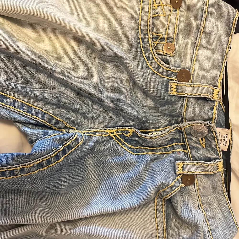 Ett par jättesnygga vitange true religon jeans i ljusblå färg med gula trådar. Jeansen är i jättebra skick och säljer för att dom inte kommer till användning (pris kan diskuteras). Jeans & Byxor.