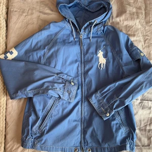 Ralph lauren jacka  - Säljer sambons Ralph lauren jacka i ljusblått. Kan såklart användas av både dam och herr.  Aldrig använd och i fint skick. Har dessvärre fått någon ljus lila fläck på baksidan av ärmen men bör gå bort i tvätten (se bild). Stl L men kan även passa M. 